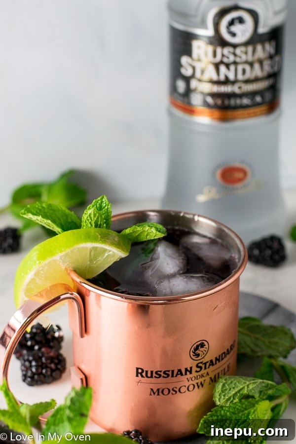 The Bramble Mule 2 Refreshing Blackberry Mint Moscow Mule cocktail in a copper mug, garnished with mint and blackberries.