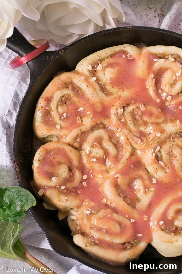 A close-up of a single Rhubarb Streusel Roll, cut open to reveal the spiral of rhubarb compote and streusel filling, with a sweet glaze drizzled on top.