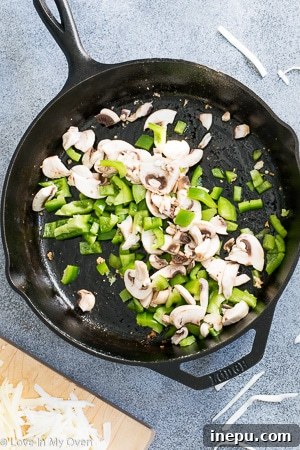 Adding shredded cheese to chorizo and vegetables in a cast iron skillet.