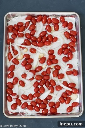 Roasted tomatoes, onions, and garlic on a baking sheet for soup