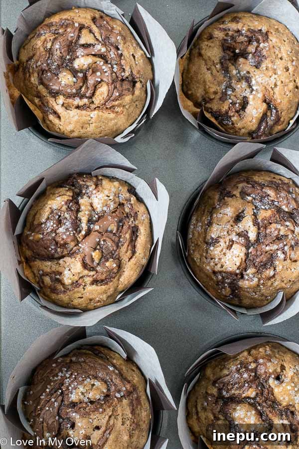Freshly baked Nutella swirl muffins with a golden crust and visible cinnamon and Nutella swirls, cooling on a wire rack.