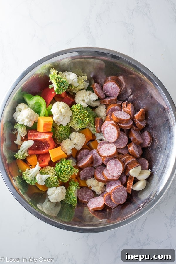 Colorful assortment of raw vegetables and sausage slices on a baking sheet, ready for roasting.