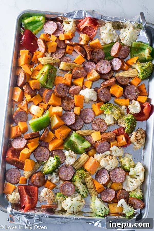 Close-up of roasted sausage and various vegetables on a sheet pan, fresh out of the oven.