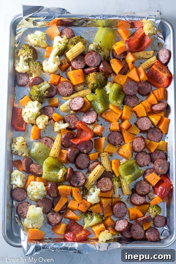 Close-up detail of roasted sausage slices and caramelized vegetables on a sheet pan.