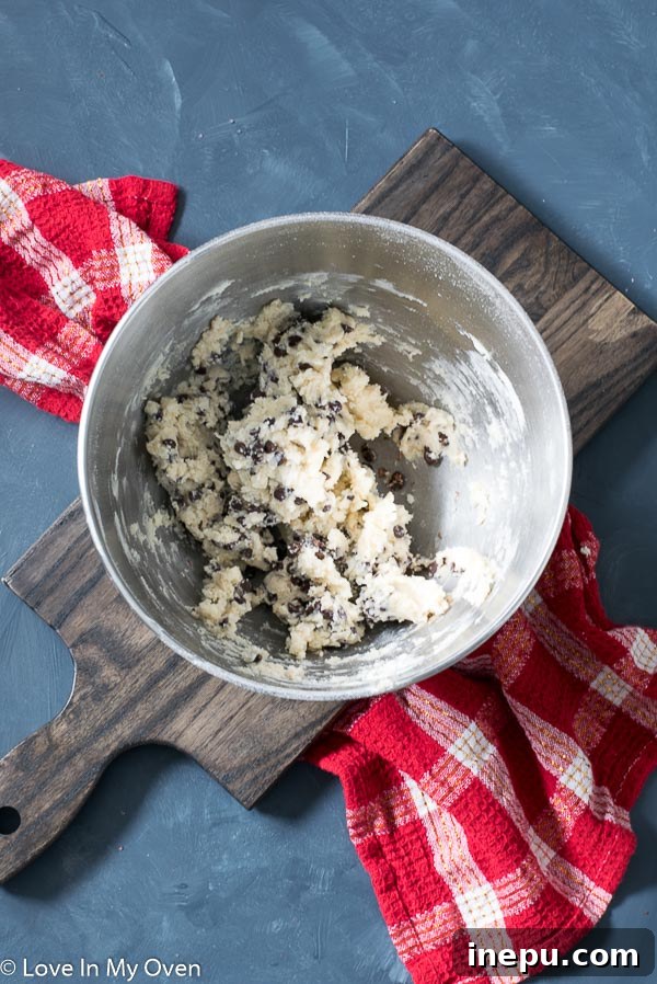 Close-up of cookie dough being rolled into perfect snowball shapes on a parchment-lined baking sheet.