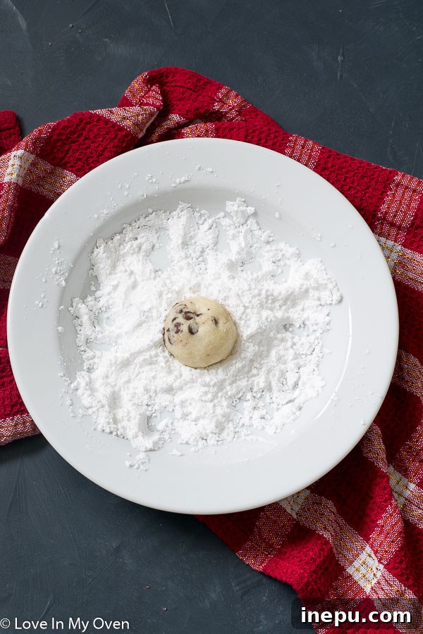 Freshly baked chocolate chip snowball cookies cooling on a rack before being dusted with powdered sugar.