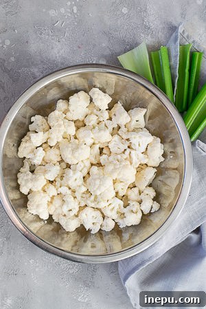 Battered cauliflower florets in an air fryer basket, mid-cooking process.