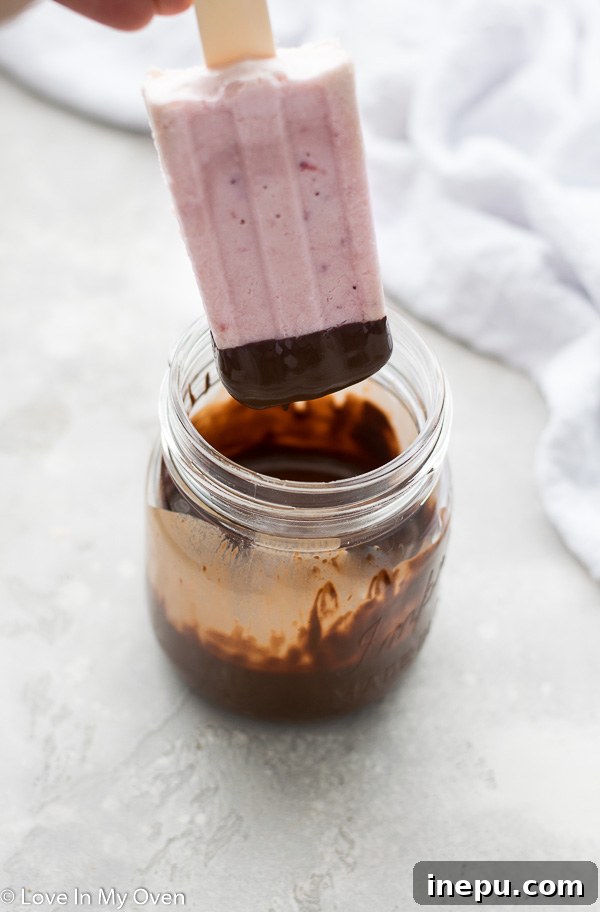 Hand placing a freshly chocolate dipped ice cream bar onto wax paper on a baking tray in the freezer