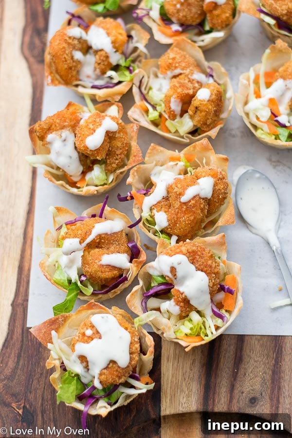 A close-up shot of an assembled Buffalo Shrimp Wonton Cup, showcasing the crispy wonton, salad, shrimp, and ranch drizzle.