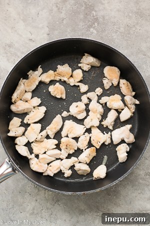 Diced chicken breast cooking in a pan alongside a pot of boiling pasta and broccoli
