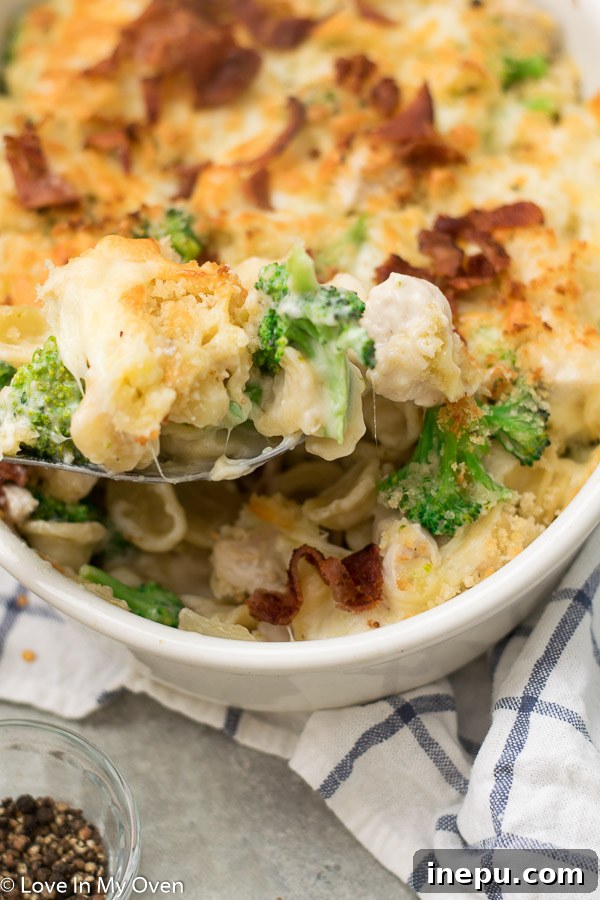 Ultimate Chicken Broccoli Pasta Casserole 8 Full casserole dish of chicken and broccoli pasta bake on a wooden table with serving spoon