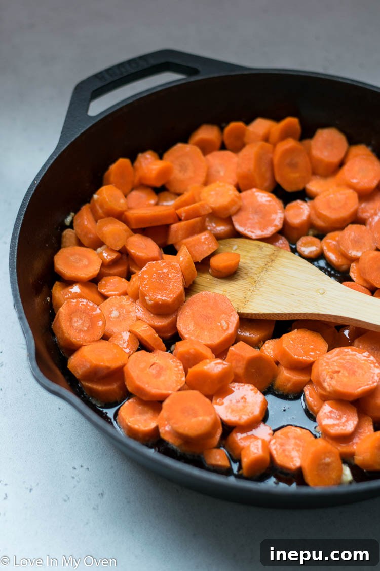 Sliced carrots being sautéed in garlic butter in a skillet