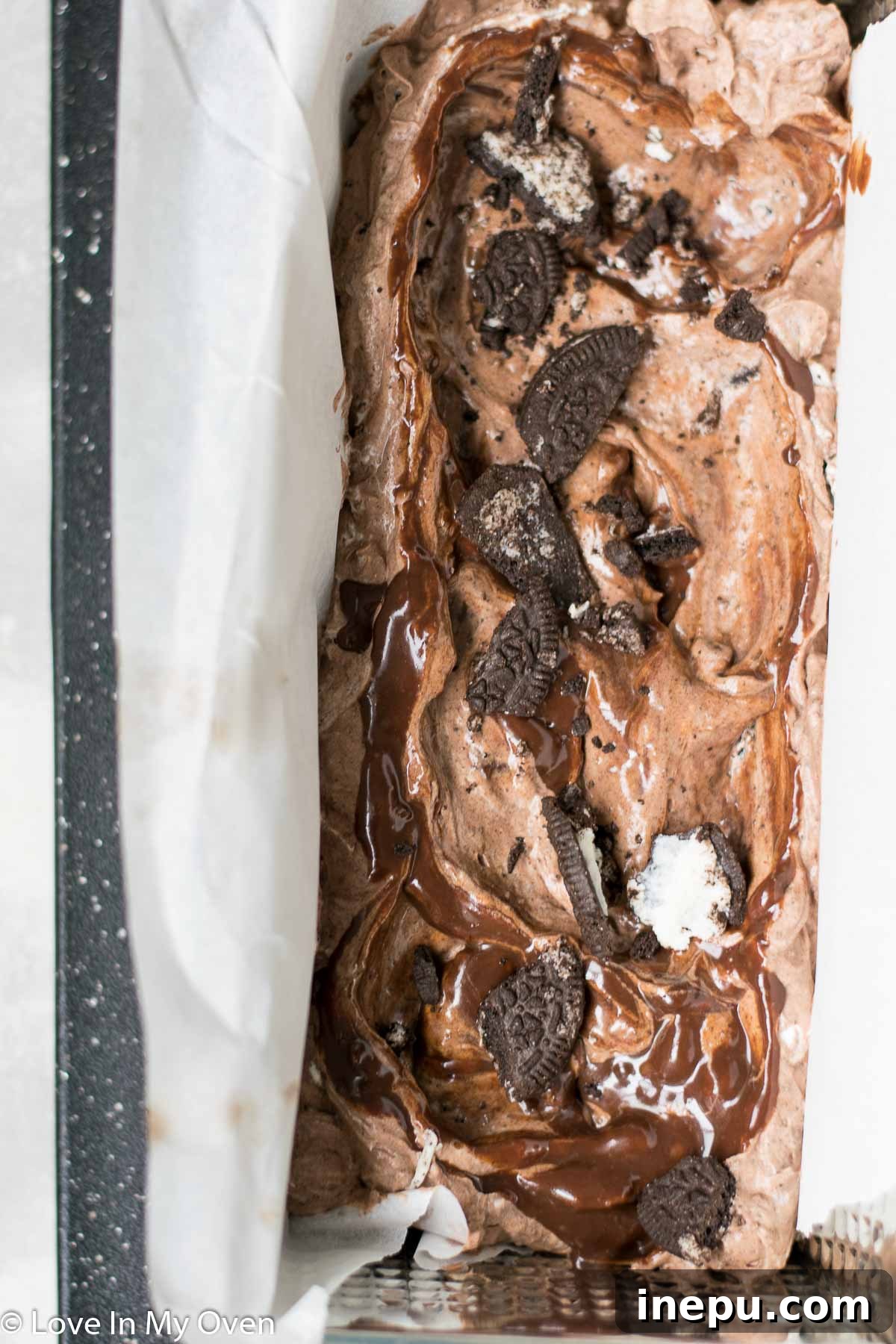 Decadent No-Churn Chocolate Oreo Delight 8 Layering chocolate Oreo ice cream mixture with chocolate ganache swirls in a loaf pan.