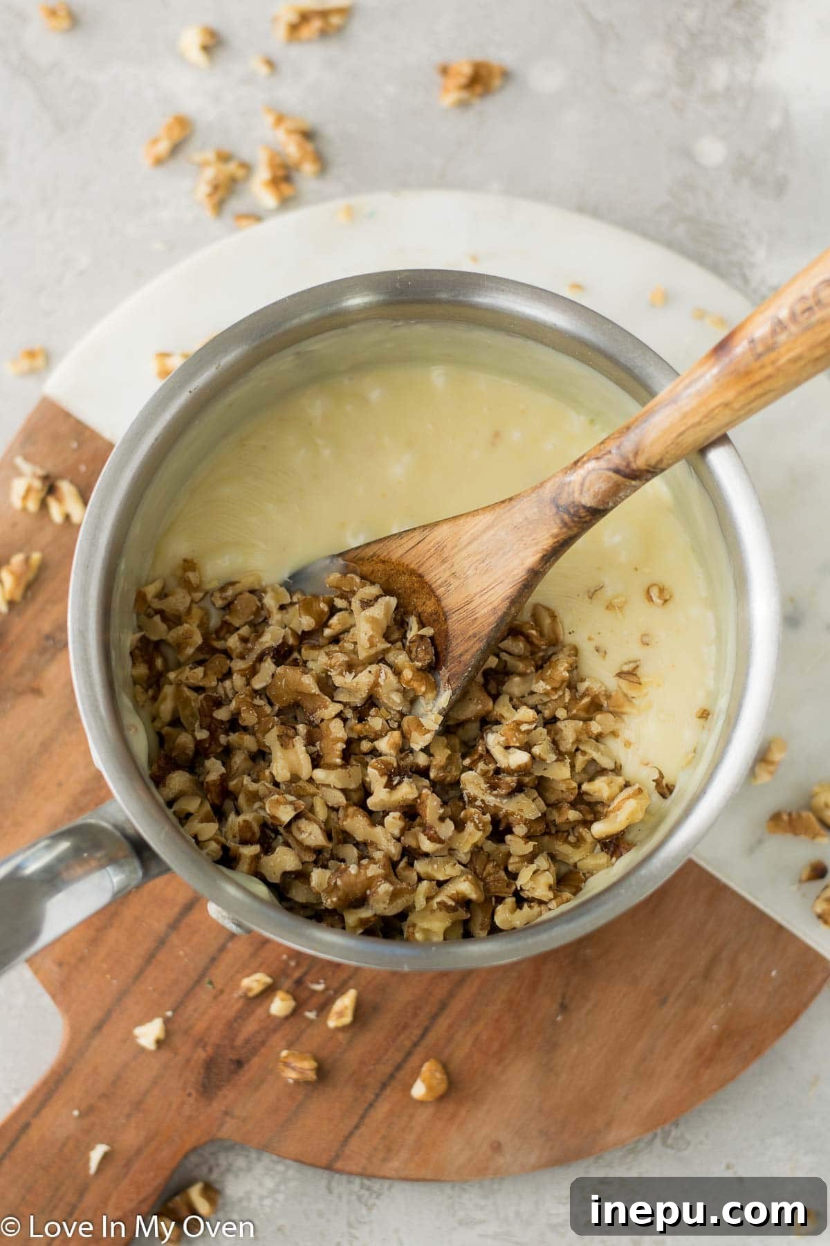 Maple extract and chopped walnuts being stirred into the melted white chocolate and condensed milk mixture.