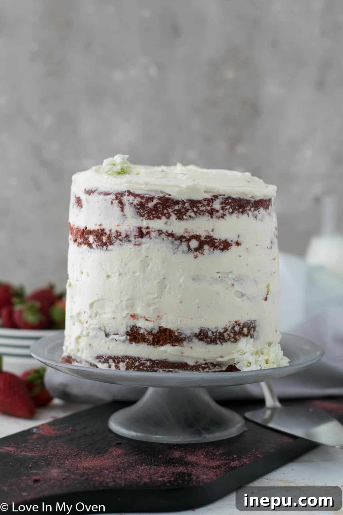 A stunning mini red velvet cake, naturally colored and topped with fluffy white frosting, sits on a cake stand.