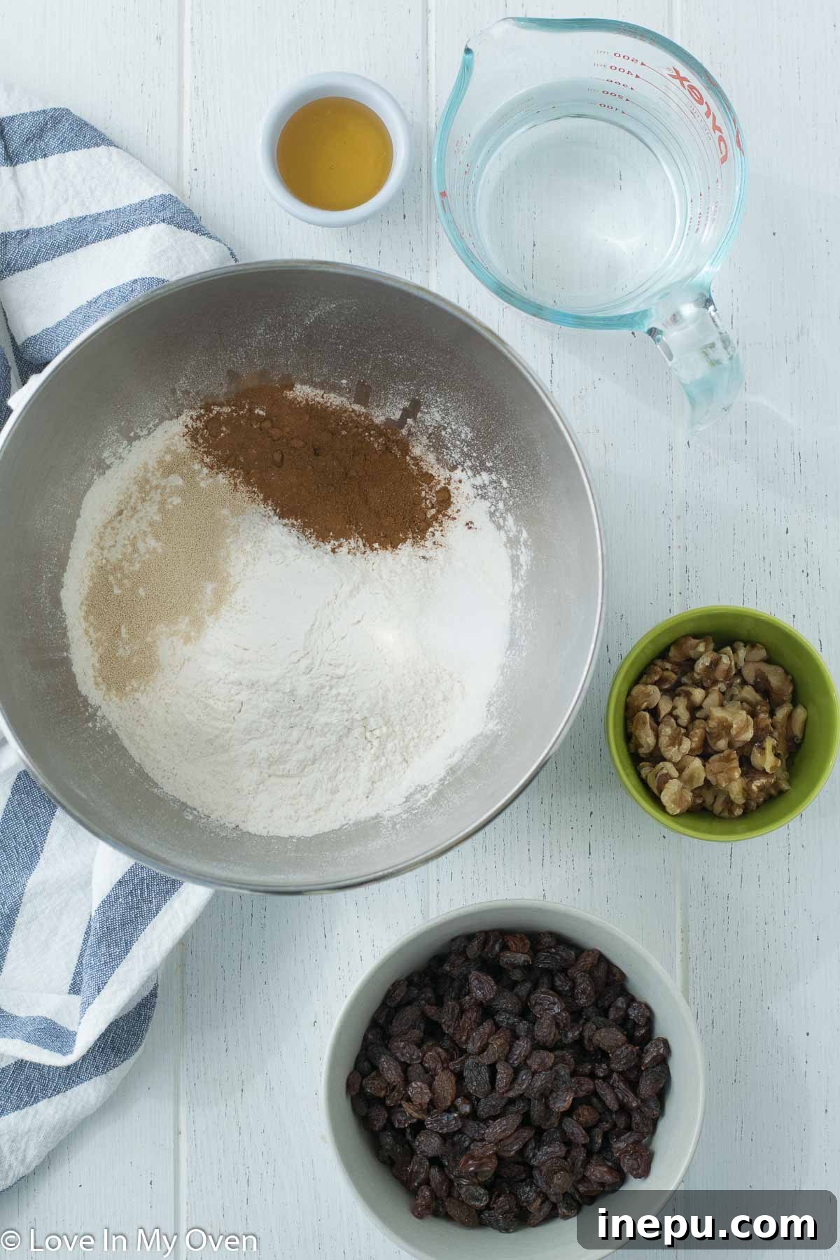 Assortment of ingredients laid out on a table for making cinnamon raisin walnut bread, including flour, yeast, cinnamon, raisins, and walnuts.