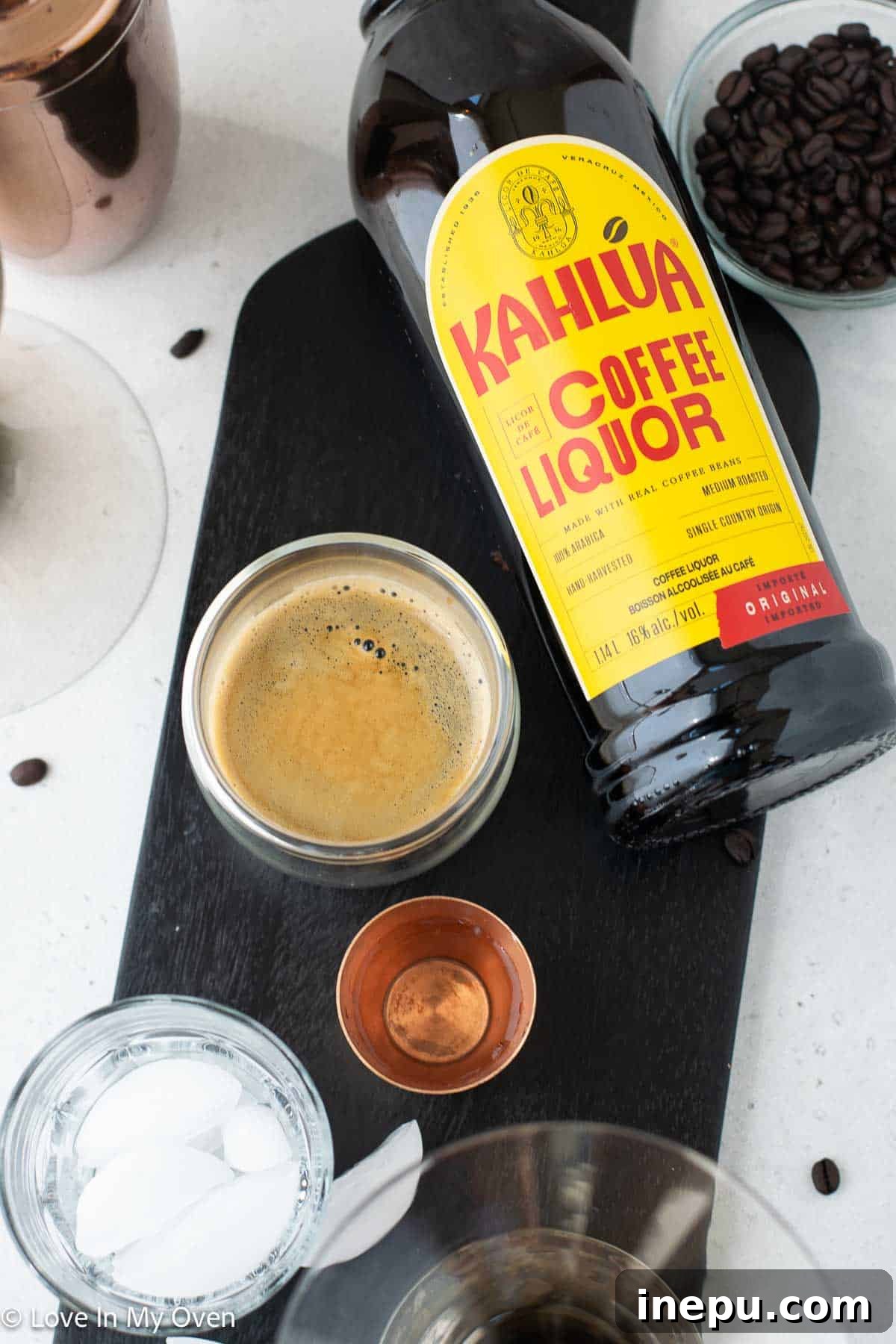 Close-up of three key ingredients: a bottle of vodka, a freshly brewed espresso shot with crema, and a bottle of Kahlua coffee liqueur, set against a dark background.