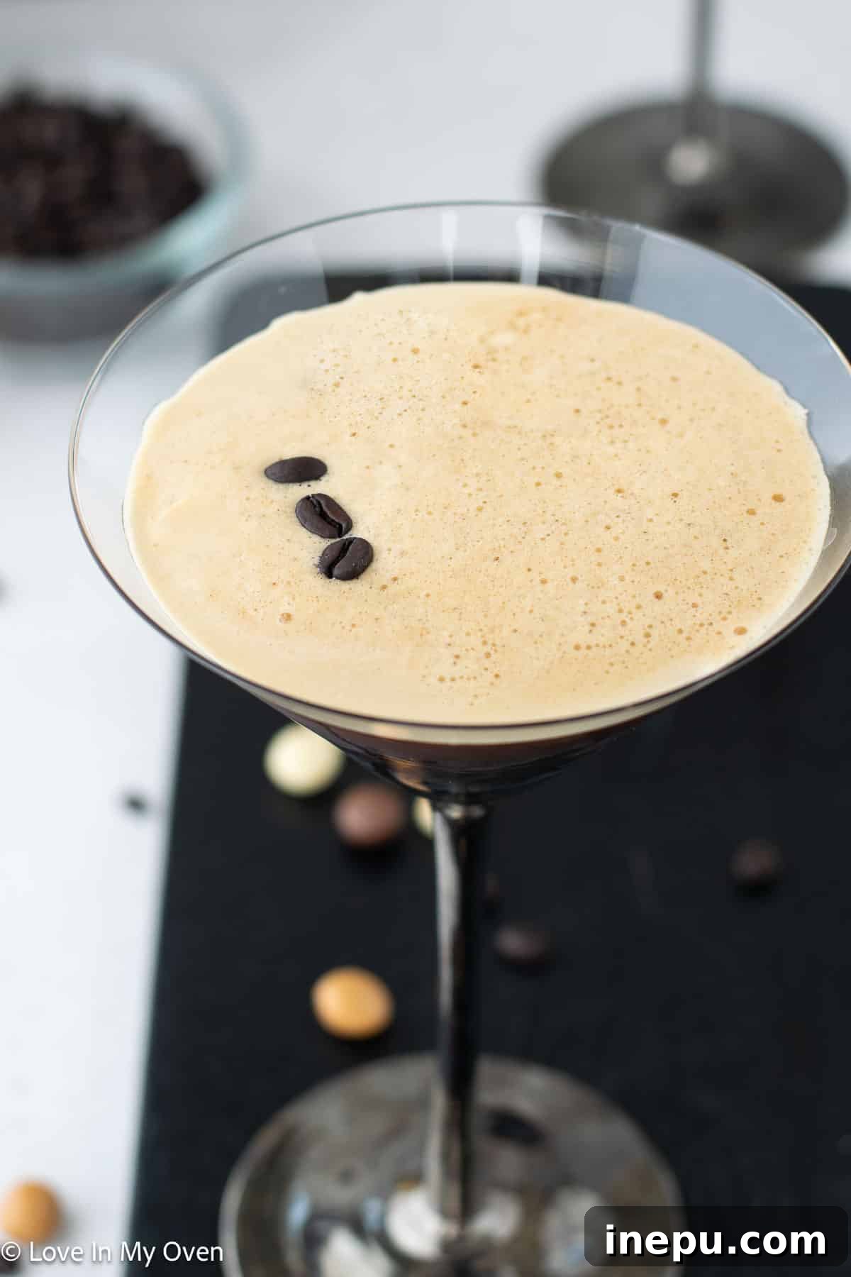 A freshly poured Vodka Espresso Martini with a thick, golden-brown foam top, garnished with three espresso beans, presented in a classic martini glass.