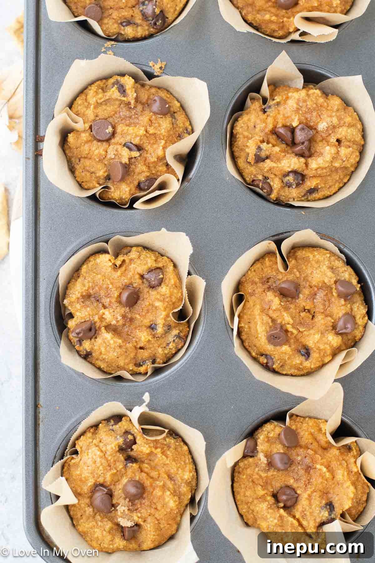 Stack of almond flour pumpkin muffins, garnished with chocolate chips and a sprinkle of powdered sugar, with some cut open to show the soft interior.
