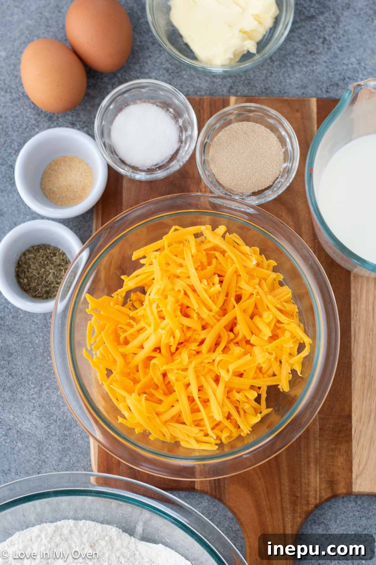 ingredients for homemade cheese rolls laid out on a counter: yeast, milk, flour, cheese, butter, eggs, and seasonings