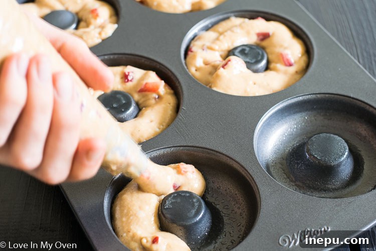 Piping strawberry donut batter into a donut pan
