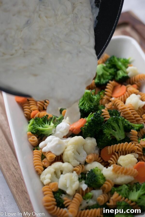 Pouring creamy sauce over mixed vegetables and pasta