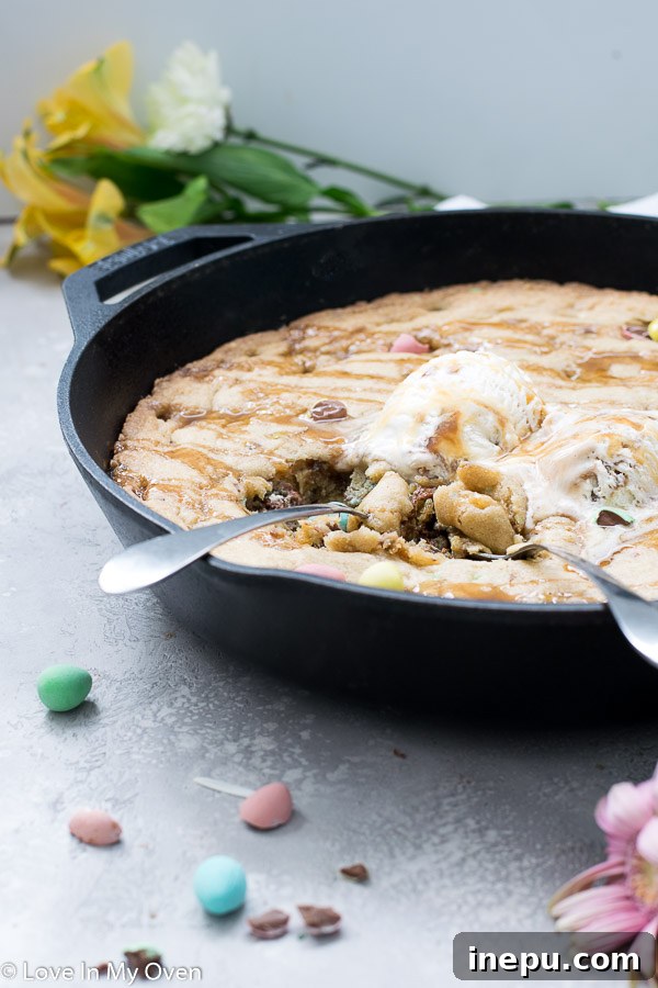 Delicious Giant Mini Egg Skillet Cookie topped with ice cream and salted caramel sauce, ready to be enjoyed.