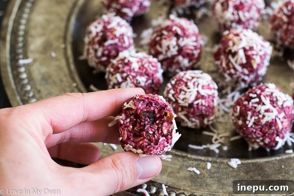 A hand reaching for a raspberry coconut bite, emphasizing their snackability and inviting nature for a quick grab-and-go treat.