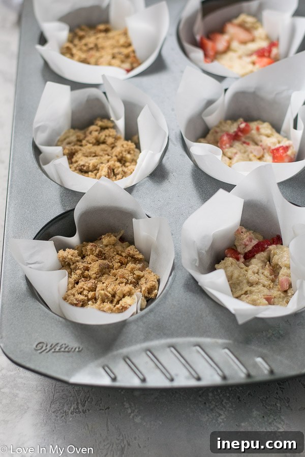 Muffin batter being scooped into jumbo muffin tin liners with streusel.
