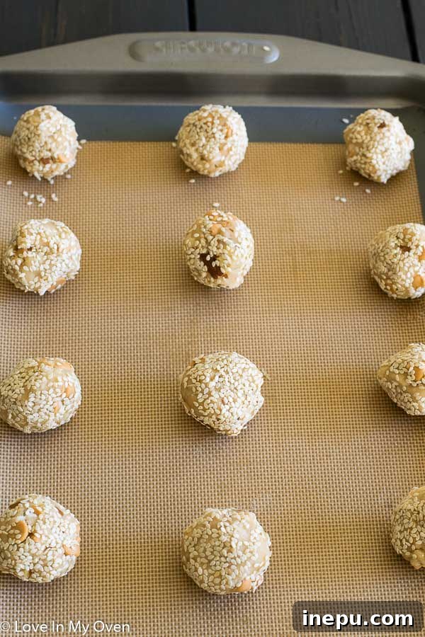 Raw cookie dough balls being rolled in sesame seeds.