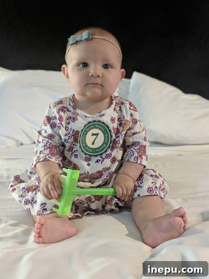 A sweet baby girl, Hattie, at 7 months old, smiling brightly and looking at the camera.